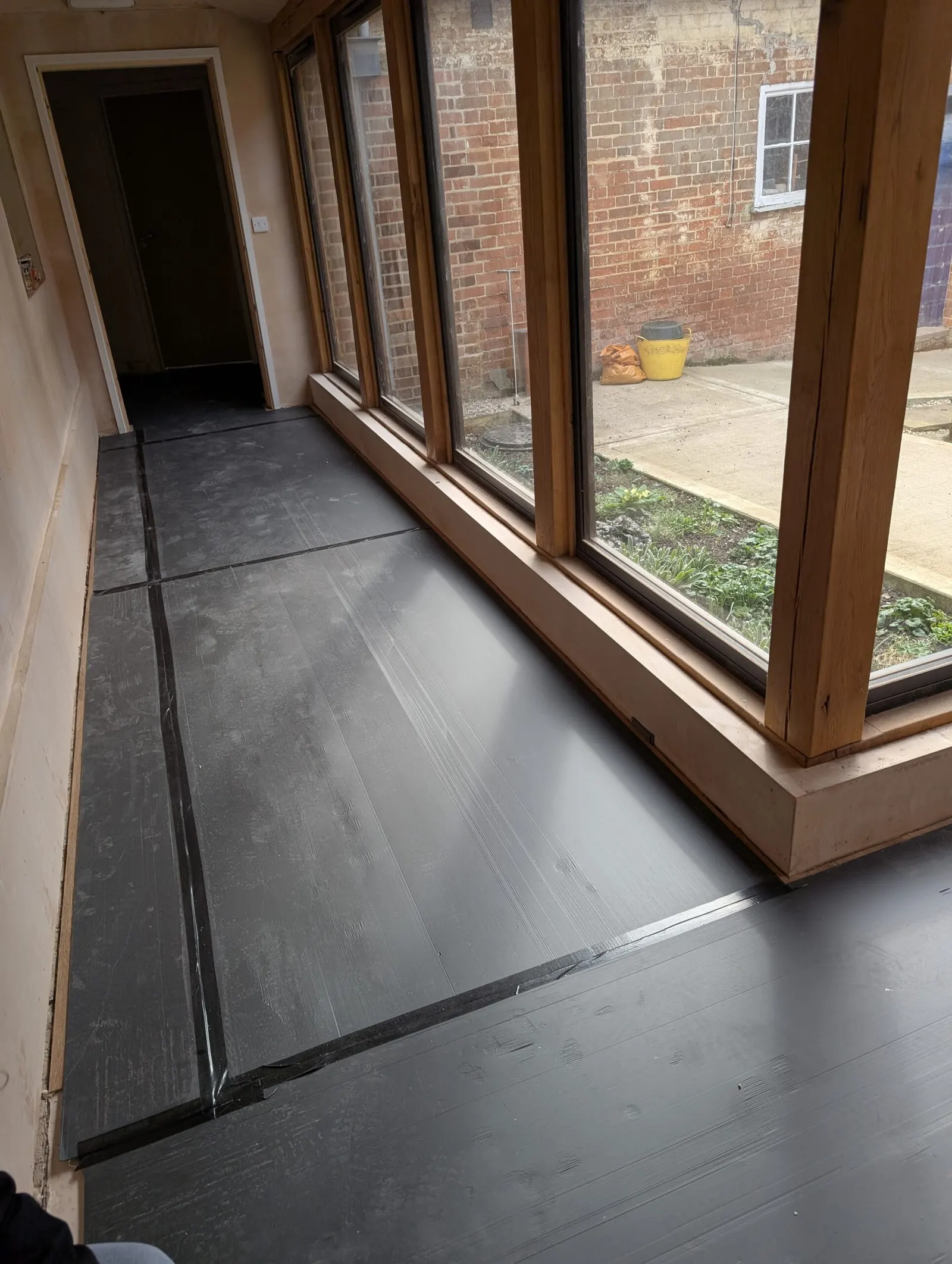 The new corridor with its floor protected during works, windows opening onto the brick courtyard